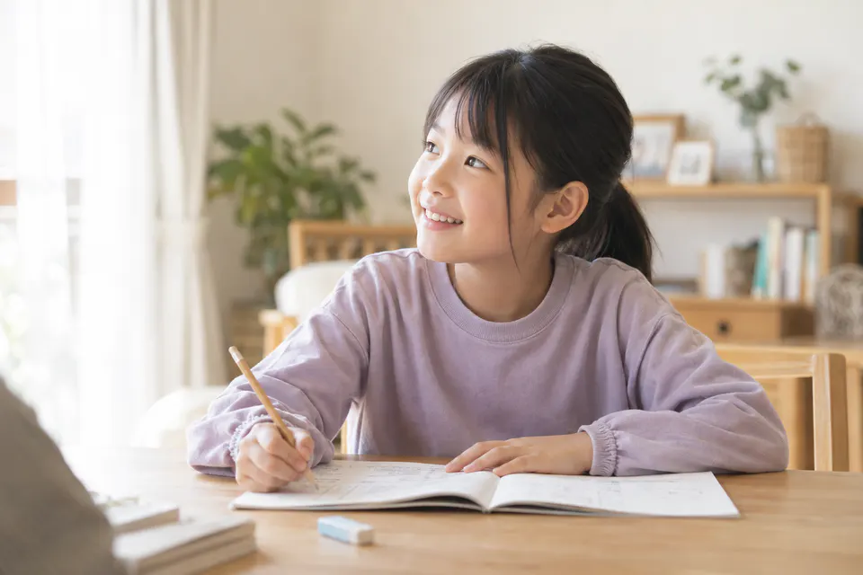 ノートに向かいながら、そばの人に自然な笑顔を向ける小学生のイメージ